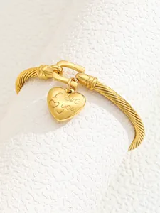 Detailed macro of a 18K gold-plated C-shaped cuff with heart charm and I love you engraving