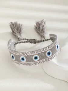 Detail of woven light gray Evil Eye bracelet with blue embroidery and tassel charms