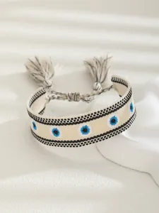 Macro detail of hand-woven lucky evil eye bracelet with white base and tassels