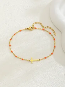 Bracelet doré avec croix et perles orange sur fond blanc avec texture douce
