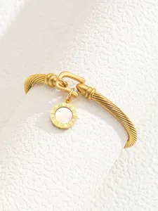 Macro detail of gold-plated bangle featuring horseshoe buckle and Roman numeral pendant