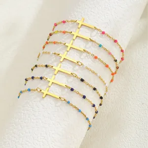 Bracelet croix en acier doré orné de perles colorées sur un support en marbre blanc