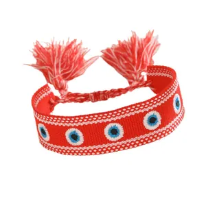 Handmade woven red evil eye bracelet with white polka dots and tassels on white background