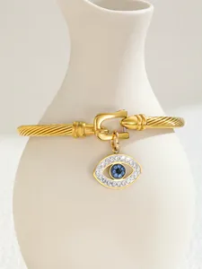 Detail view of 18K gold-plated C-shaped cuff bracelet with evil eye charm on a white vase