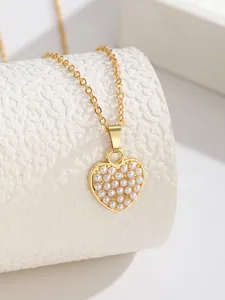 Vue détaillée d'un pendentif cœur doré orné de micro perles sur un support texturé blanc