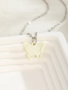 Macro view of light yellow butterfly pendant on a silver metal chain over white stand