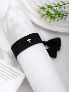 Detail of embroidered cross pattern on black woven bracelet with tassels