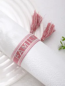 Macro shot of pink embroidered tassel bracelet featuring a silver FAMILY letter design