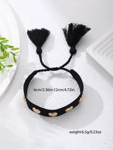 Detail view of woven black bracelet with gold heart charms and fringe tassels