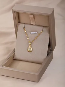 Detalle de collar de gota dorada con piedra blanca y motivos de ojo en caja de regalo
