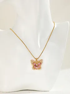 Detail of a gold butterfly necklace with pink gemstones and white pearls on a white bust