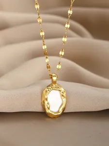 Detail of gold necklace with oval mother of pearl pendant on elegant silk fabric