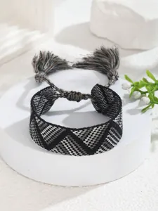 Detalle de pulsera tejida geométrica con borlas y cierre ajustable en colores gris y blanco