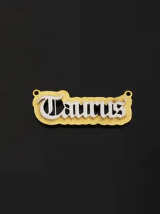 Macro shot of gold and silver Taurus zodiac pendant with glitter texture and gothic font