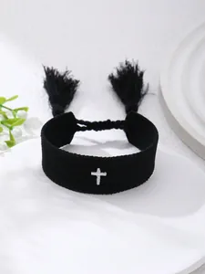 Vista de detalle de pulsera tejida negra con cruz blanca bordada y borlas colgantes