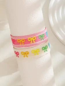 Detalle de pulseras tejidas rosa y crema con lazos bordados de múltiples colores
