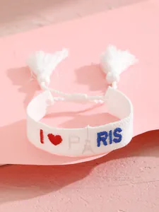 Detalle de pulsera de tela tejida con bordado I Love Paris y pompones blancos