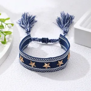 Pulsera tejida azul con estrellas doradas y borlas sobre fondo blanco minimalista