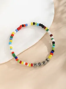 Detalle macro de cuentas de colores y colgantes HOPE en una bandeja de cerámica