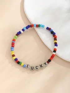 Detalle macro de pulsera de cuentas de colores con letras LUCKY sobre fondo beige