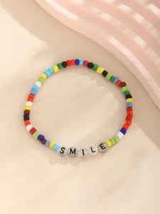 Detalle de pulsera de cuentas de colores con letras SMILE sobre fondo beige suave