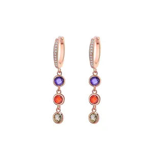 Detail of rose gold dangle earrings featuring bezel-set purple, red and green gemstones