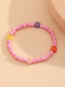 Detalle de pulsera de cuentas de colores con dijes de corazón, flor y luna sobre rosa
