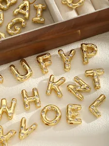 Macro shot of 26 puffy gold letter pendants with zircon stones on leather and wood background