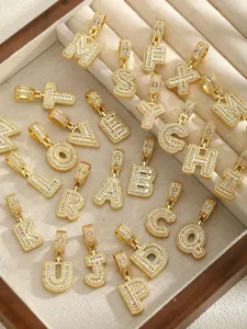 Détail macro de pendentifs alphabet plaqués or 18k avec zircons dans une boîte à bijoux