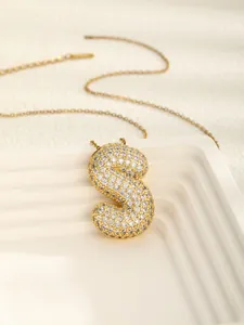 Close-up of golden letter S pendant necklace with shimmering white zircon stones