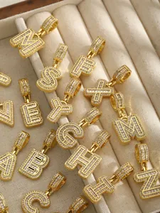 Détails de pendentifs lettres dorés sertis de zircons sur un plateau de velours