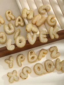 Macro detail of gold balloon letter charms with micro-pave white zircon inlay