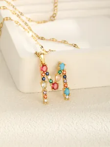 Macro shot of gold-plated M letter pendant with vibrant colorful zircon stone inlays