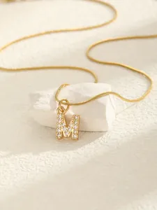 Détail macro du pendentif lettre M doré avec zircons sur fond de pierre