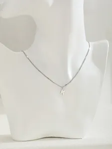 Primer plano de un collar de acero inoxidable pulido con un colgante de la letra K en un busto