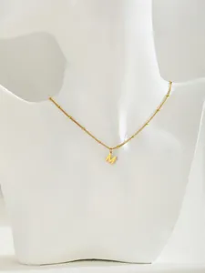 Primer plano de un collar con colgante de letra M dorada en una cadena de satélite minimalista