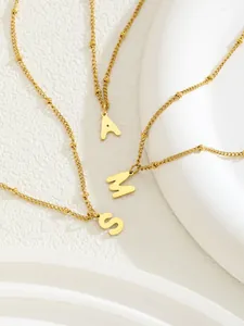 Detalle de los colgantes de letras A M S doradas en una cadena de bolas minimalista