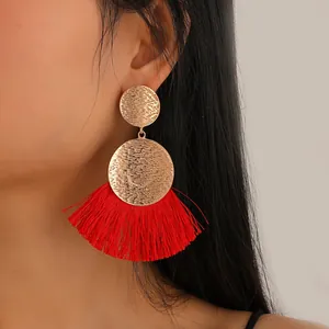 Bohemian gold metal fan-shaped earrings with red tassels on a female model