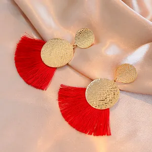 Hammered gold fan earrings with long red tassels on luxury champagne silk background