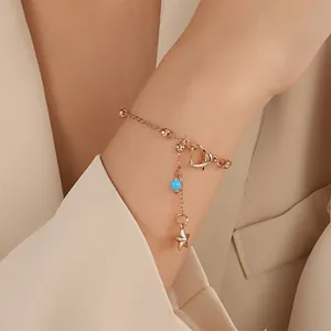 Detail von Roségold Herz-Fußkettchen mit blauer Perle und poliertem Stern-Anhänger am Handgelenk