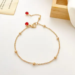 Detail einer Gold-Fußkette mit Herzverschluss und leuchtend roten Edelsteinanhängern