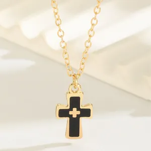 Collier croix dorée minimaliste avec émail noir présenté sur d'élégantes marches beige