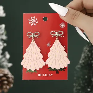 Pink Christmas tree earrings with golden bows and polka dots on a holiday card