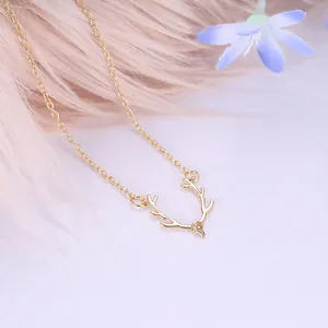 Minimalist golden elk antler pendant necklace with small crystal on a soft pink background