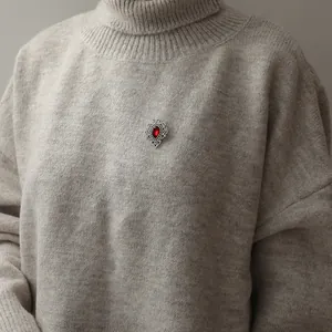 Vintage Victorian style silver brooch with red teardrop gemstone on a grey sweater
