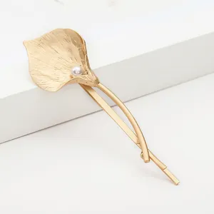 Elegant gold Calla Lily hair clip with pearl accent on a minimalist white pedestal