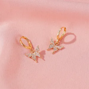Boucles d'oreilles papillon dorées élégantes avec cristaux de zircon sur fond de soie rose