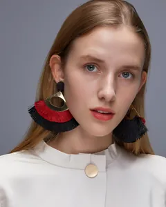 Close-up of bohemian fan-shaped earrings with red and black tassels on a gold metal base