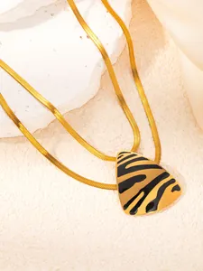 Close-up of golden snake chain with triangle leopard print pendant on silk fabric