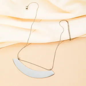 Gepolijste waaiervormige stalen hanger aan een slangenketting op een beige zijden stof